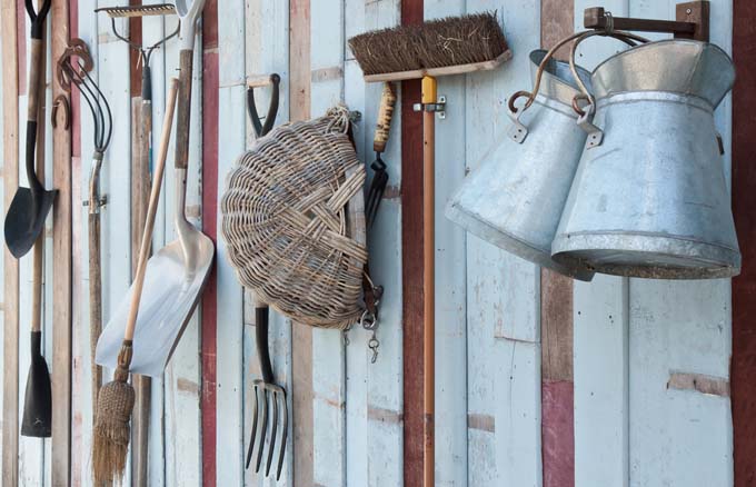 A close up of a shed wall showing garden tools neatly hanging from individual hooks, creating a tidy appearance.