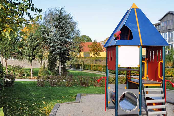 A children's playground with a colorful playset in a summer garden with houses and trees in the background.
