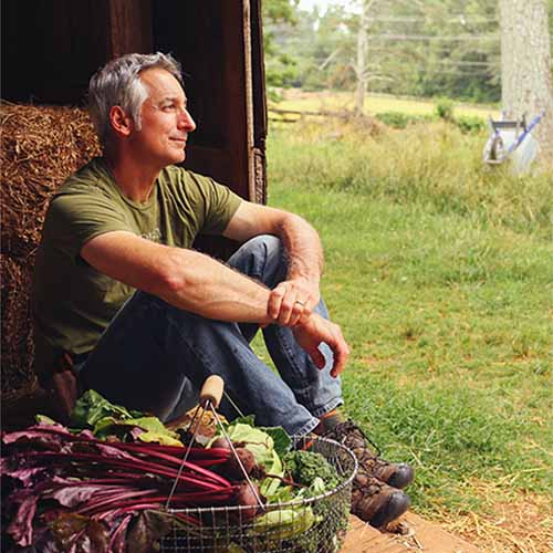 A close up square image of Joe Lamp'l sitting on a step with a basket of freshly harvested produce next to him.
