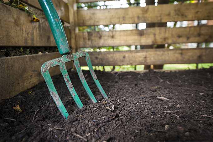 A green pitchfork rests in a pile of brown compost.