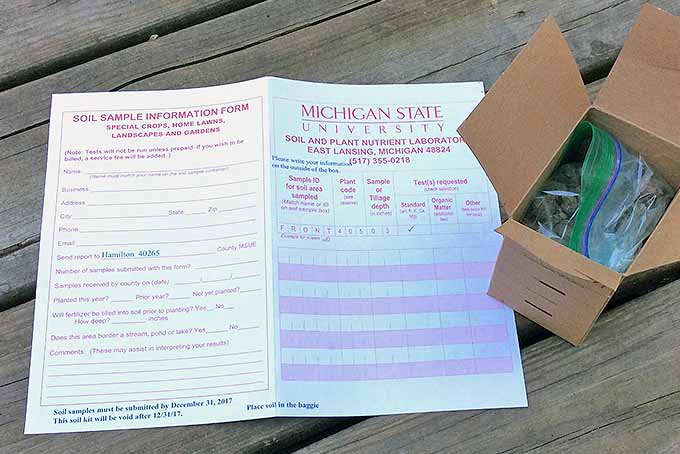 Together on a rough, wooden platform, a box filled with a bag of dirt and a pamphlet rest. The paper contains information and blank spaces for the users to send in their samples to be analyzed at a lab at Michigan State University.