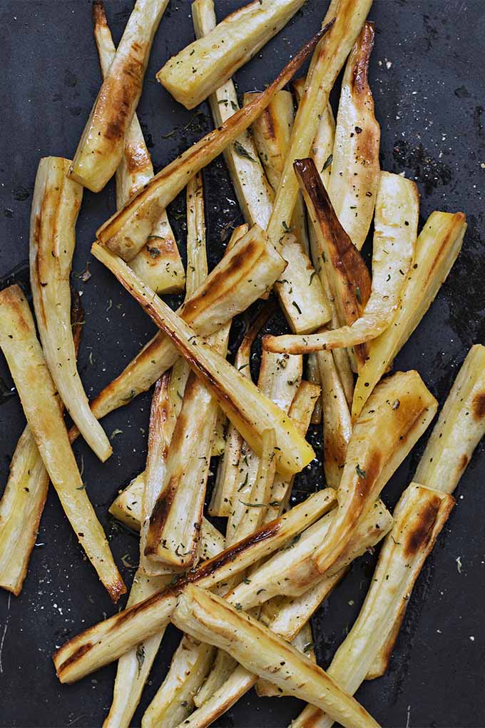 Vertical top-down image of caramelized parsnip fries on a black baking pan.