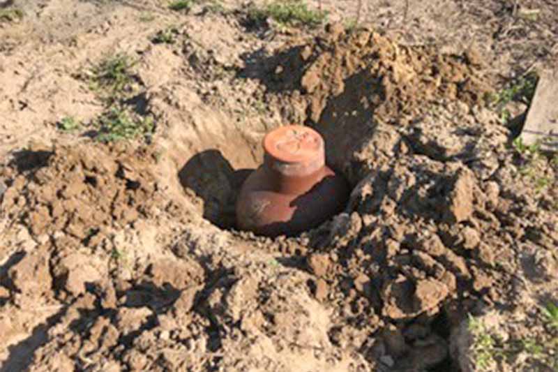 A terra cotta olla is being buried in brown soil.