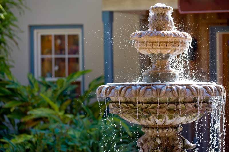 A close up horizontal image of a garden fountain in the front of a residence.