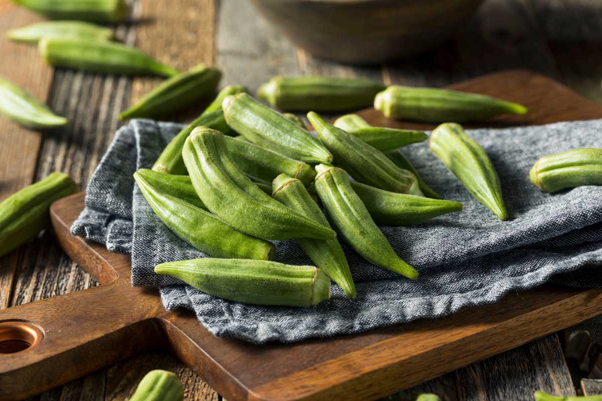 Freshly harvest okra on a blue kitchen towel on a small wooden cutting board.