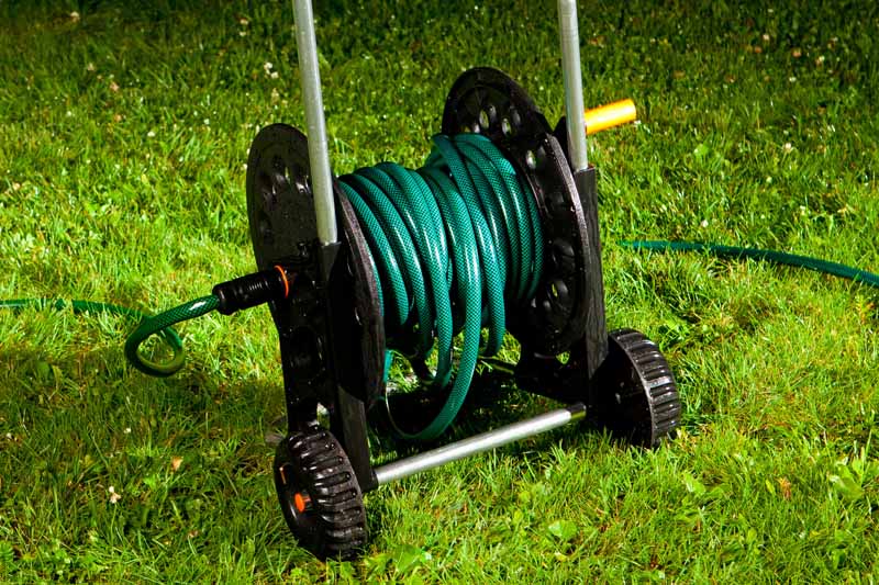 A mobile garden hose reel on wheels on green grass.