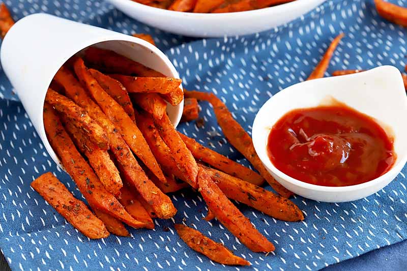 A batch of homemade cajun flavored sweet potato fries on a blue table cloth.
