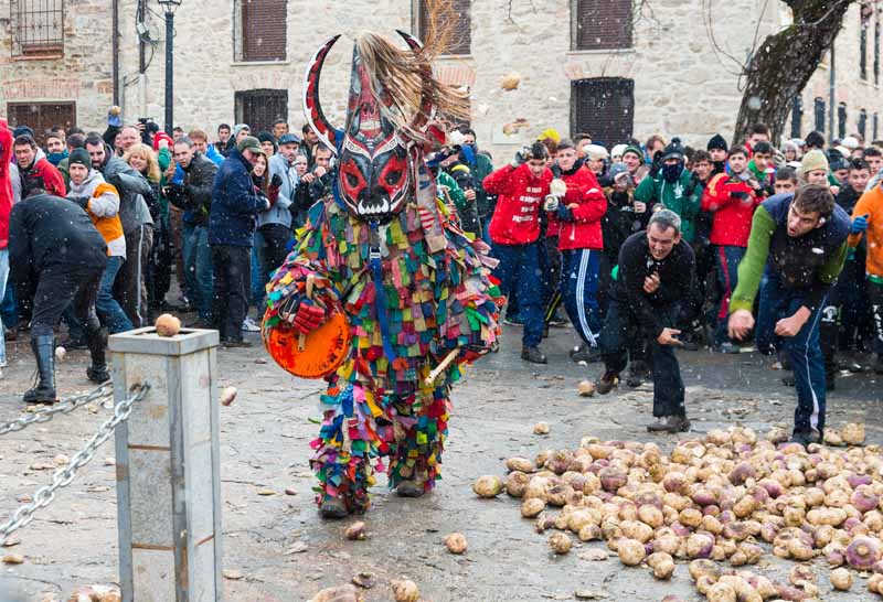 A man dressed up in a multicolored devil suit is subjected to being pelted with turnips at the Jarramplas Festival.