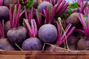 A wooden box containing harvested beets, the soil cleaned off them and the stems cut about two inches above the root. The roots are a deep purple, contrasting with a little of the green foliage still attached and the bright purple stems.