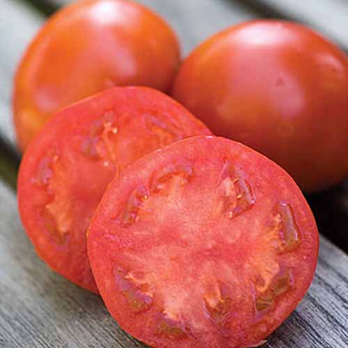 A close up of a 'Sweet Seedless' variety of tomato, cut in half, with two whole fruits in the background, on a wooden surface.