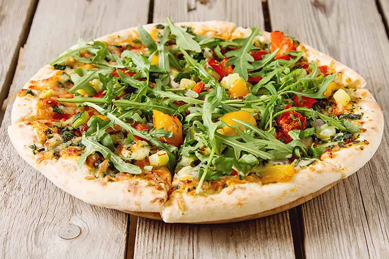 A close up of a pizza with fresh arugula on the top, set on a wooden table.