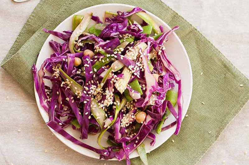 A close up of a white plate containing purple cabbage slaw freshly prepared, set on a green fabric mat on a wooden surface.