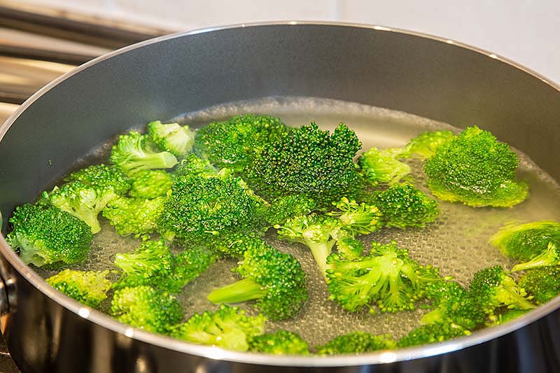 A close up of a metal saucepan with boiling water and bright green broccoli florets.