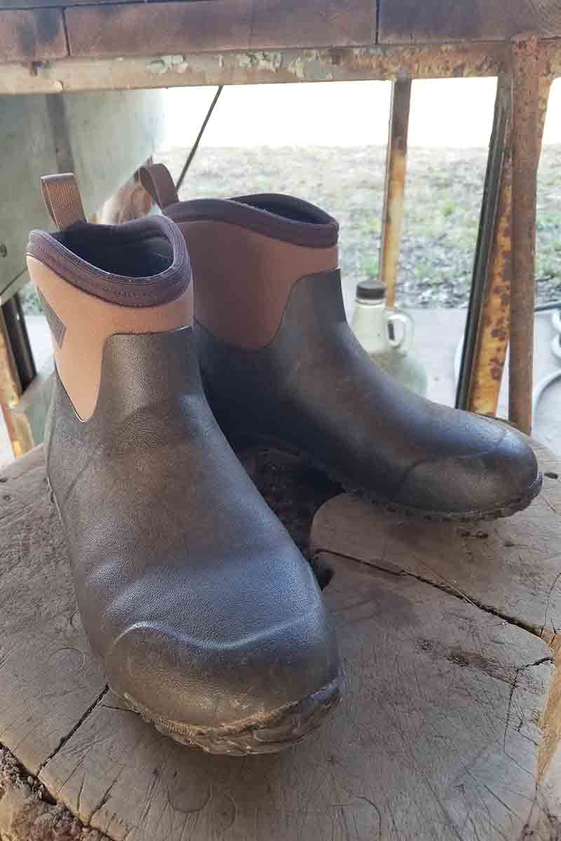 A close up of a pair of two tone brown gardening boots set on a wooden surface with a view out of the window in the background.