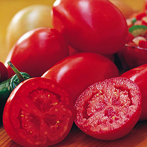 A close up of the 'Fresh Salsa' variety of tomato, one of them cut in half, set on a wooden surface.