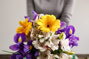 A close up of a fresh bouquet of cut flowers with a woman in a gray sweater in soft focus in the background.