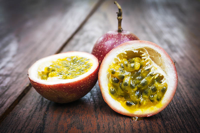 A close up of a ripe passion fruit that has been cut in half and set on a dark wooden surface.