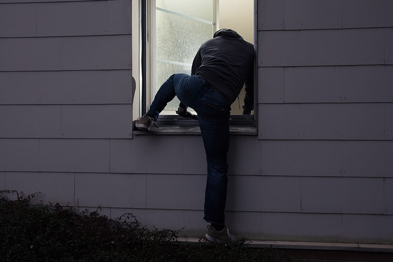 A back view of a man climbing into a house through the window in the dark.
