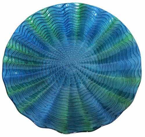 A close up of a shimmering blue-green glass bird bath with ridged interior.