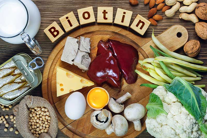 A close up of a wooden chopping board containing a variety of foods rich in biotin, set on a wooden surface.