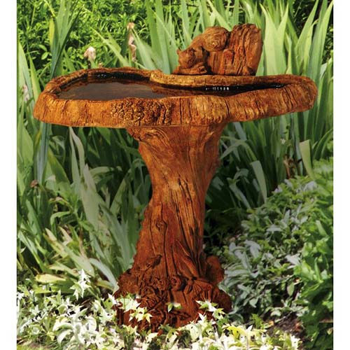 A close up of a cast stone bird bath made to look as though it is carved from wood, set in a garden border.