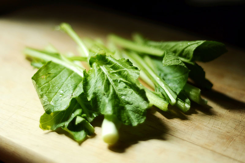 A close up of green leaves set on a wooden chopping board in the kitchen on a dark soft focus background.