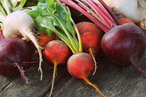 A horizontal image of red, golden, and white beetroots freshly harvested and set on a wooden surface.