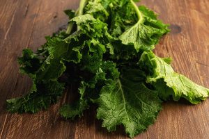 A close up horizontal image of freshly harvested turnip greens set on a wooden surface.