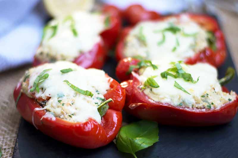A close up horizontal image of freshly baked stuffed red peppers set on a dark gray surface.