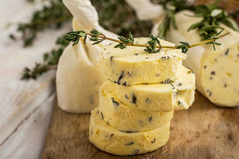 A close up horizontal image of herb butter slices set on a wooden surface pictured on a soft focus background.