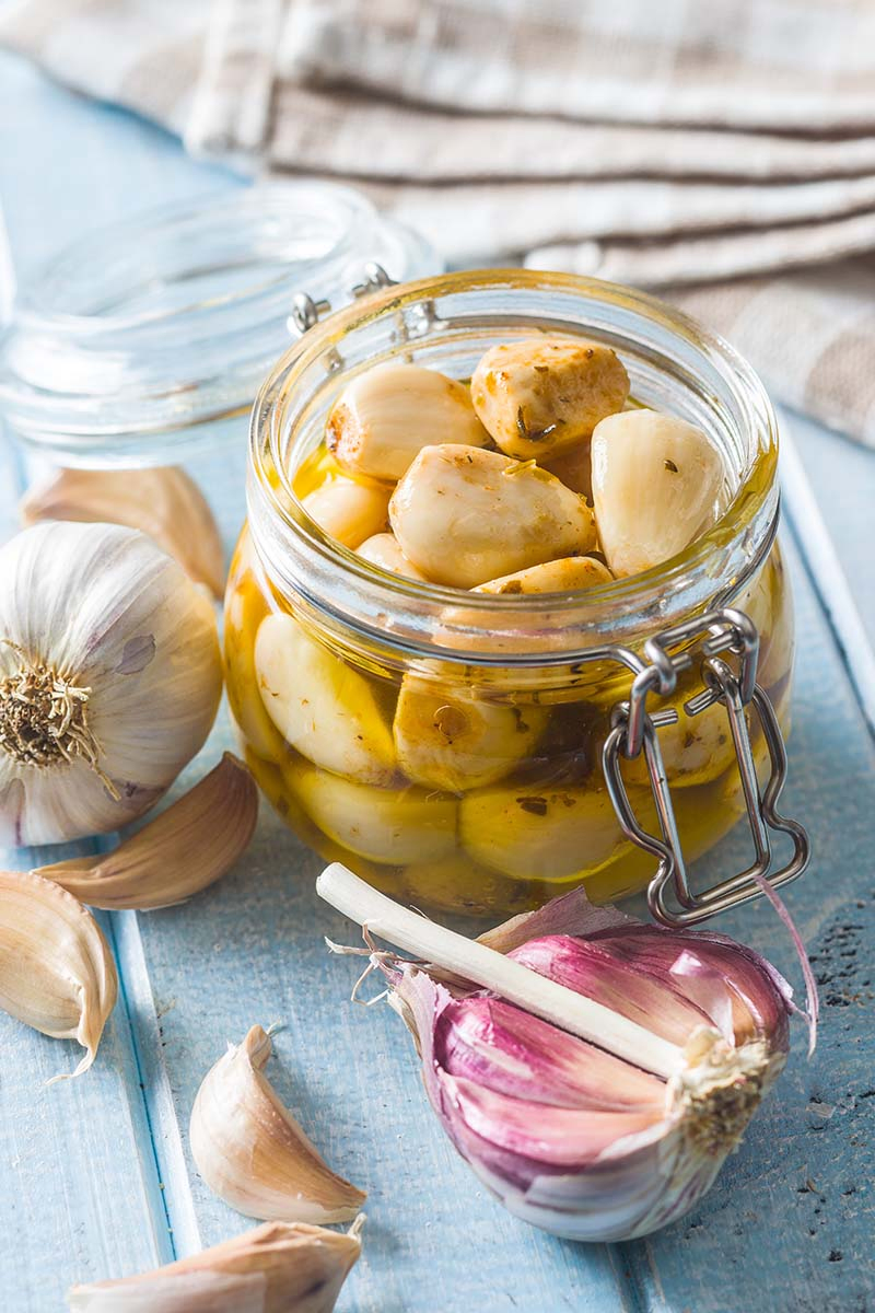 A close up vertical image of a jar of pickles set on a wooden surface with fabric in soft focus in the background.