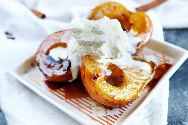 A close up horizontal image of a plate of baked caramelized pears topped with fresh cream and caramel sauce.