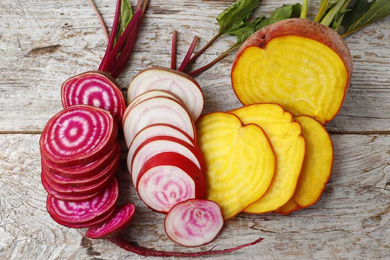 A close up horizontal image of sliced striped and yellow beets set on a wooden surface.