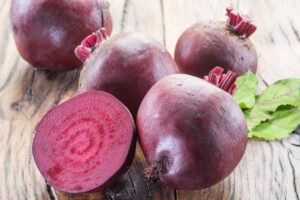 A close up horizontal image of deep red beetroots freshly harvested and cleaned and set on a wooden surface.