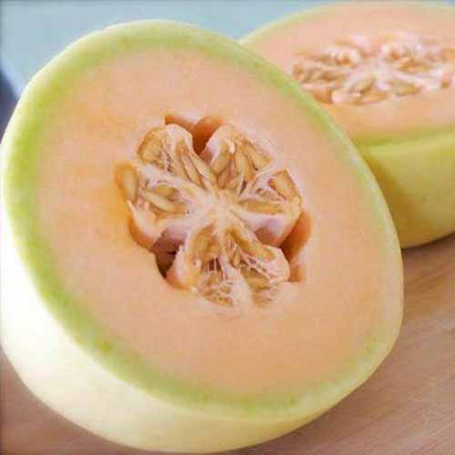 A close up square image of a 'Honeydew Orange' melon cut in half and set on a wooden surface.