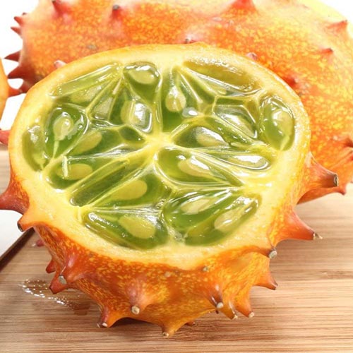 A close up square image of a Kiwano jelly melon cut in half and set on a wooden surface