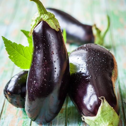 Four black beauty eggplant fruit stacked on a rustic table.
