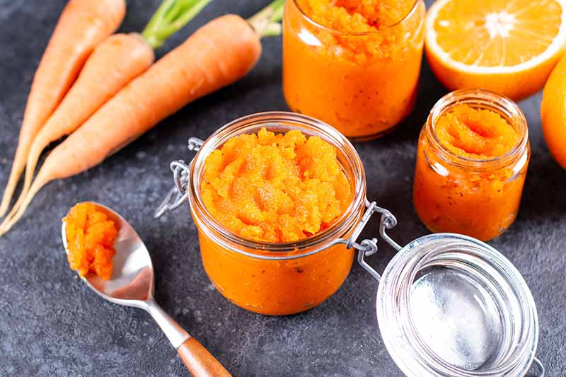 A close up horizontal image of a variety of jars filled with homemade carrot, orange, and habanero jam.