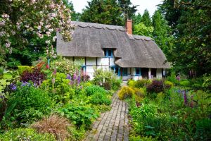 Cottage garden with center pathway leading to a rustic style Tudor home with a thatched roof.