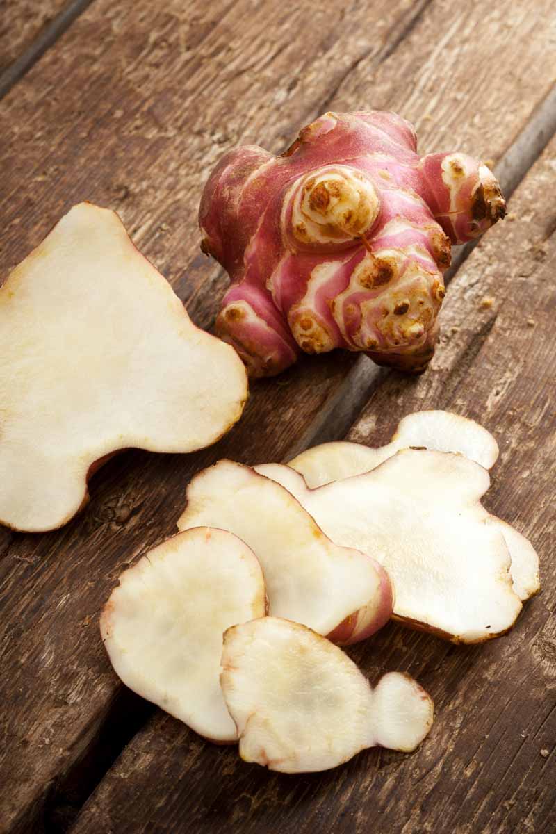 A close up vertical picture of sliced Jerusalem artichokes set on a wooden surface.