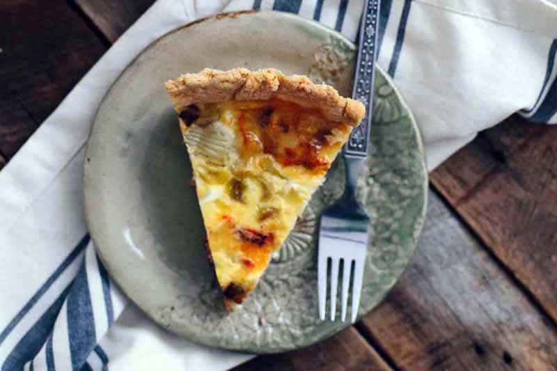 A close up top down image of a slice of freshly made quiche on a green plate set on a wooden surface.