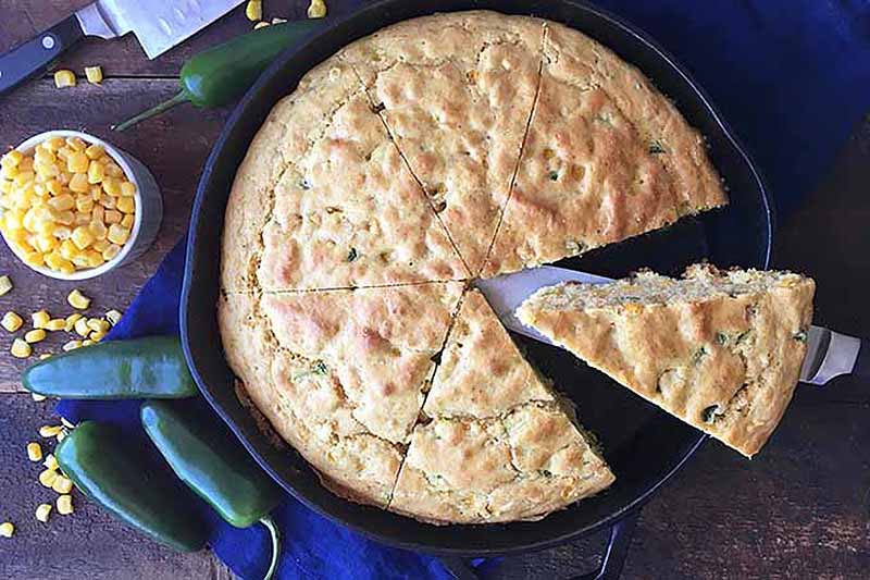 A horizontal top down image of a skillet of freshly prepared jalapeno cornbread set on a wooden surface.