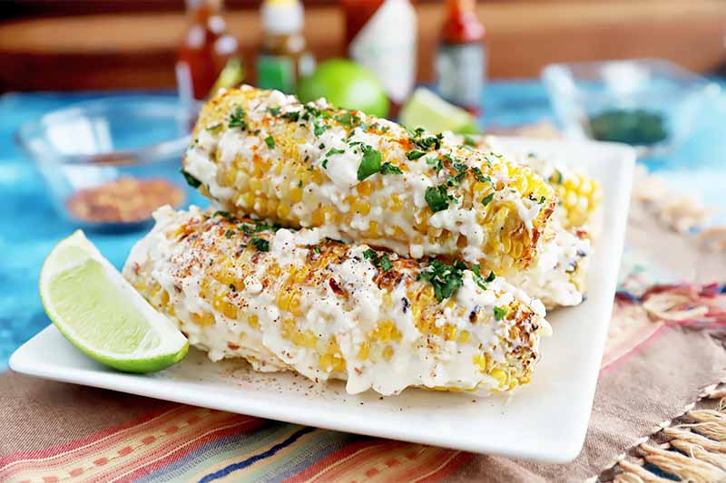 A close up horizontal image of Mexican sweet corn on a white plate with a slice of lime on the side.