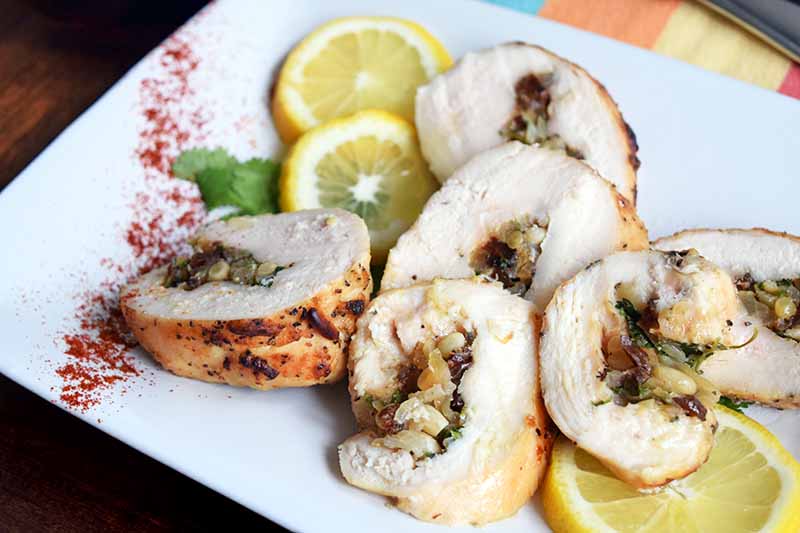 A close up horizontal image of freshly cooked chicken roulade on a white plate with lemon slices.