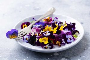 Edible flowers including violets and pansies on a plate.
