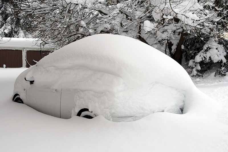 A close up horizontal image of a car covered in a thick blanket of snow.