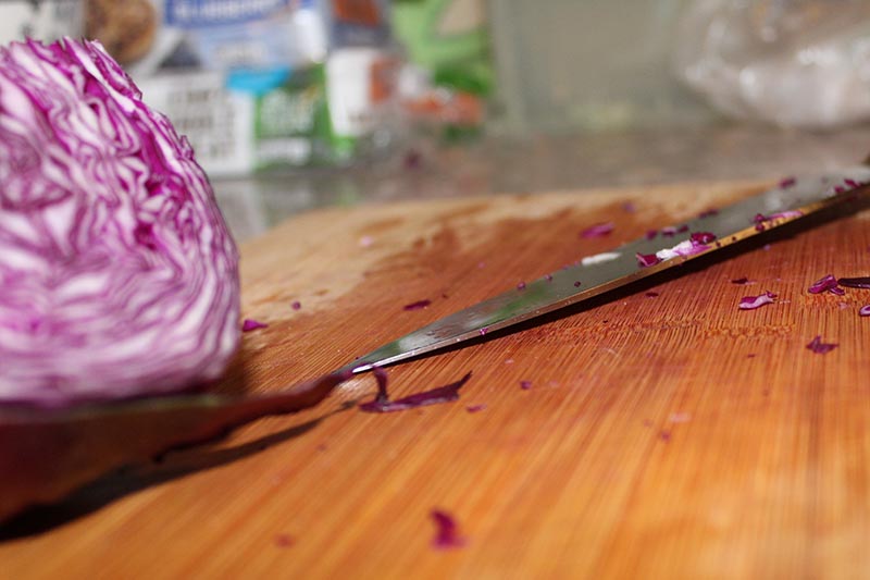 A close up horizontal image of a half of red cabbage set on a wooden chopping board with a knife.