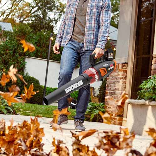 A close up square image of a gardener using the Worx WG584 Leaf Blower on a patio.