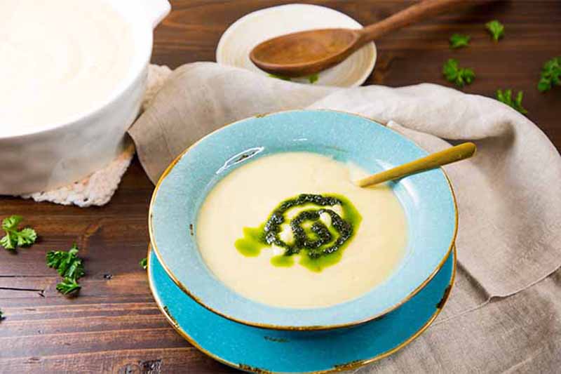 A close up horizontal image of a cream of celery root soup in a blue bowl set on a wooden surface.
