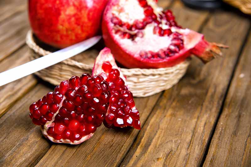 A close up horizontal image of a whole and cut open pomegranate set on a wooden surface.